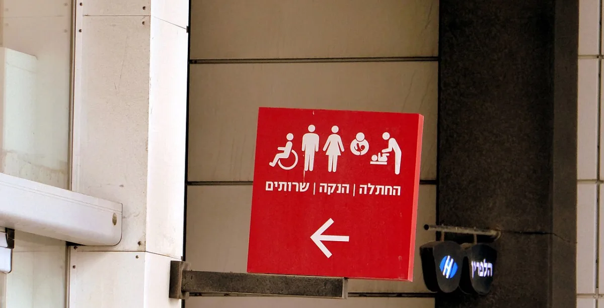 Rood bewegwijzeringsbord met toiletpictogrammen, tekst en een pijl naar links